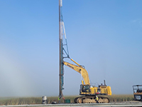 Workers use machines to put towering metal wick into place at work site.